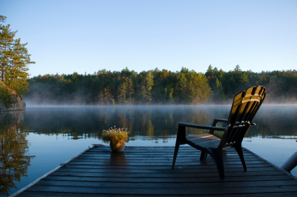 A chair on a dock facing a serene lake.